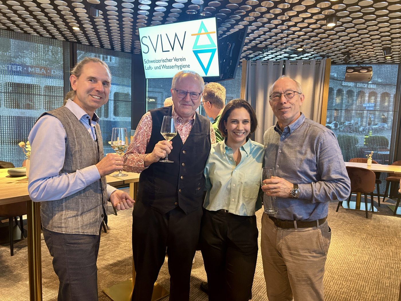 Vier Teilnehmende mit Gläsern vor dem SVLW-Logo